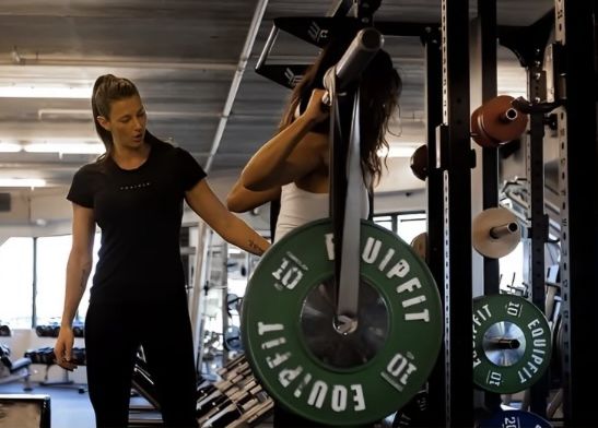 Jordanna coaching a client through a supported barbell squat