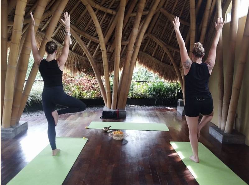 Two women practising yoga in a bamboo pavilion on an AlignHER retreat